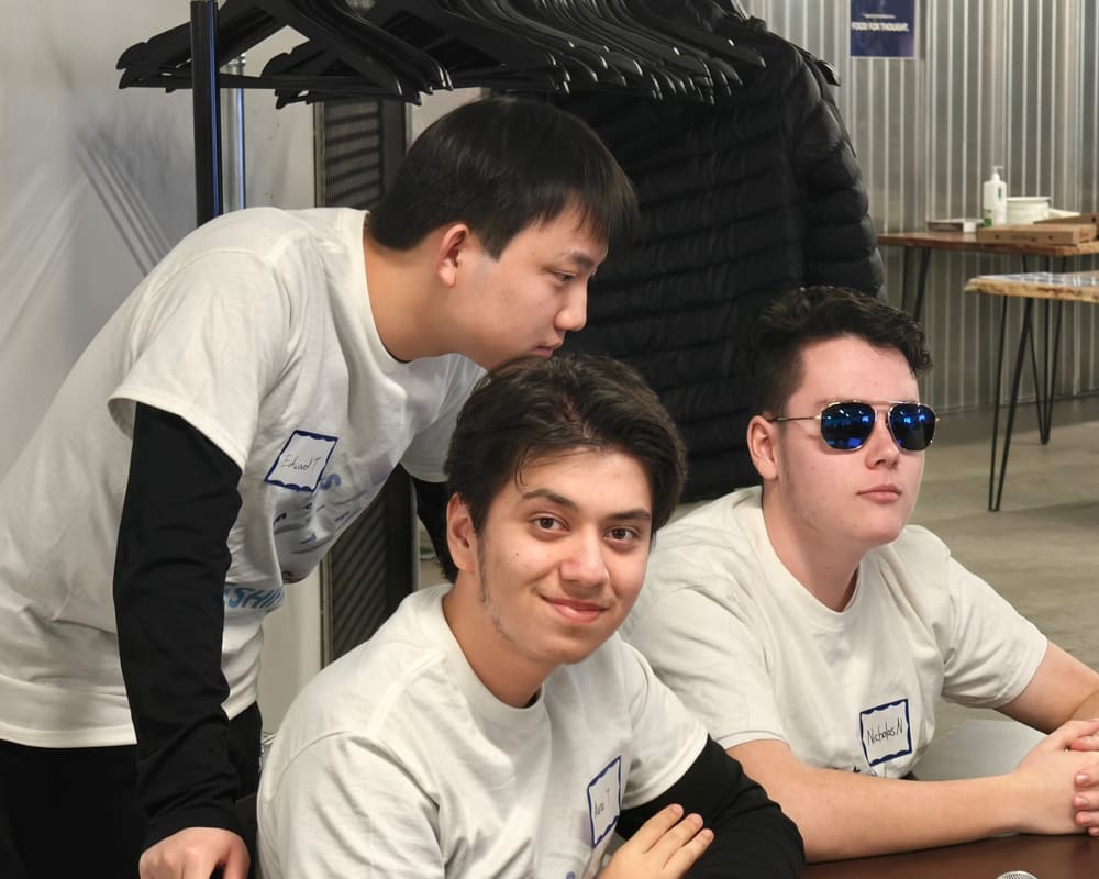 Three students in TypeShift shirts at a workshop, one smiling at the camera